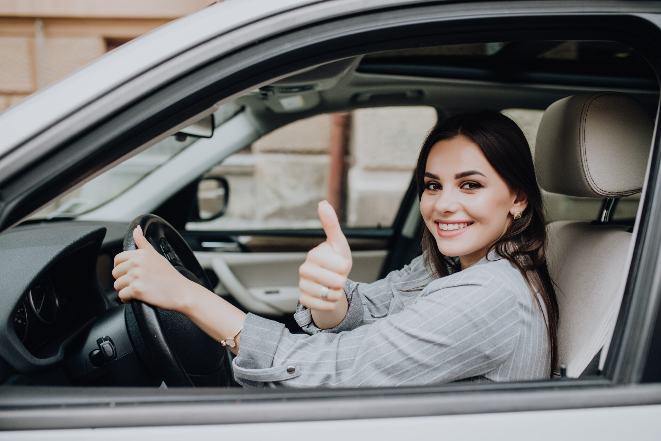 Beautiful young woman driving her brand new car and showing her thumb up